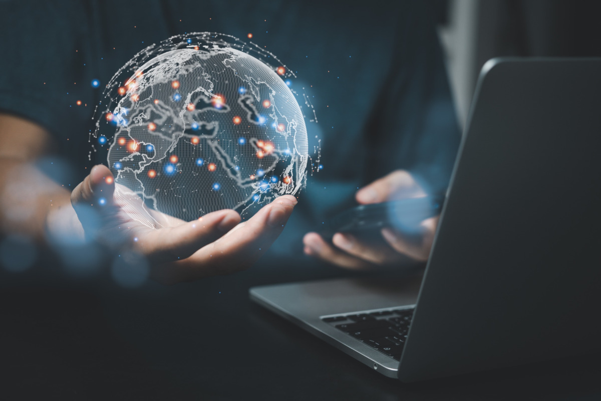 Man holding digital globe and mobile phone while looking at a laptop